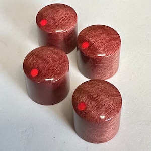 Puede incluir: Cuatro pomos de madera con un punto rojo en el centro. Los pomos son de color marrón rojizo con un patrón de veta de madera.