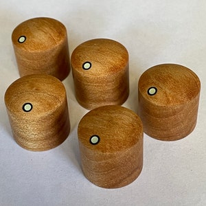 Puede incluir: Cinco perillas cilíndricas de madera con acabado marrón claro. Cada perilla tiene una pequeña incrustación circular verde claro. Las perillas están dispuestas en un patrón ligeramente disperso, mostrando su diseño simple pero elegante.
