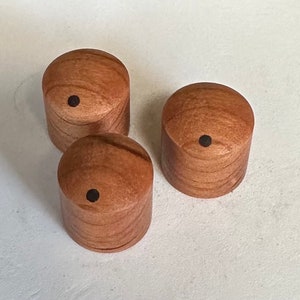 May include: Three wooden knobs with a black dot in the centre. The knobs are a light brown colour with a wood grain pattern.