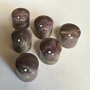 Puede incluir: Seis pomos de madera con un patrón de veta de madera púrpura y gris y un punto blanco en el centro.
