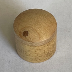 Puede incluir: Un pomo de madera clara con un pequeño agujero en el centro. El pomo es redondo y tiene una superficie lisa.
