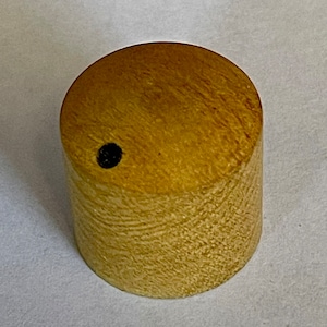 May include: A light brown wooden knob with a small black hole in the centre.