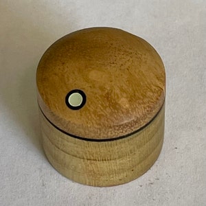 Könnte beinhalten: Eine kleine, runde Holzkiste mit hellbrauner Oberfläche. Der Deckel hat einen weißen Kreis mit schwarzem Rand in der Mitte.