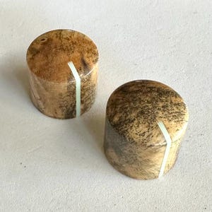 May include: Two wooden knobs with a white line inlay. The knobs are brown and have a natural wood grain pattern.