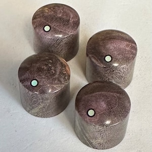Puede incluir: Cuatro pomos de guitarra de madera púrpura y gris con puntos blancos en el centro.