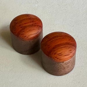 May include: Two wooden knobs with a reddish-brown top and a darker brown base. The knobs have a wood grain pattern.