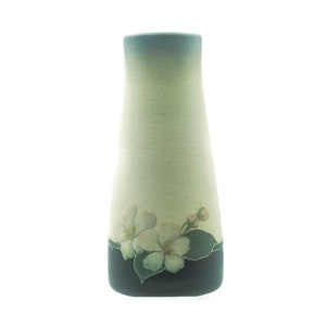 Pode incluir: Um vaso de cerâmica com um esmalte verde claro e azul. O vaso tem um desenho floral com flores brancas e folhas verdes ao redor da base.