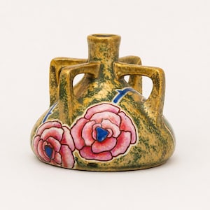 Op de afbeelding: Een decoratieve keramische vaas met een gouden afwerking en vier handvatten. De vaas heeft roze rozenillustraties met blauwe centra en blauwe accenten. De vaas is ongeveer 15 cm hoog.