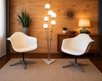 May include: Two white molded shell chairs with black trim and silver metal swivel bases, positioned on either side of a tall floor lamp featuring six spherical glass globes on thin metal stems rising from a triangular marble base.