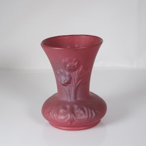 May include: A matte red vase with a flared top and a rounded base. The vase features embossed floral designs on the body and neck. The vase is approximately 6 inches tall.