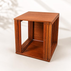 May include: A square, wooden side table with a warm, reddish-brown finish. The table has an open, box-like design with vertical supports and a solid top and bottom. The dimensions are approximately 18 inches wide, 18 inches deep, and 18 inches high.