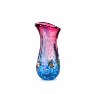May include: A colorful glass vase with a flared top. The vase features a gradient of colors, transitioning from a deep pink rim to a light blue base. Decorative fish motifs are visible near the base. The vase is approximately 8 inches tall.