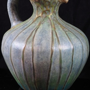 May include: A green and blue ceramic jug with a textured surface and a wide, rounded body. The jug has a handle and a spout.