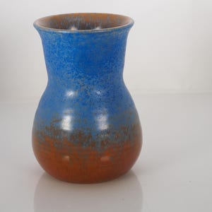 May include: A ceramic vase with a blue and orange color scheme. The upper portion of the vase is blue, transitioning to orange at the base. The vase has a rounded body and a flared rim, suitable for floral arrangements.