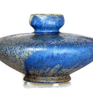 May include: A blue ceramic vase with a unique shape. The vase has a wide, flat body and a small, cylindrical neck. The surface is textured with a speckled pattern in shades of blue and gold. The vase is a decorative item.