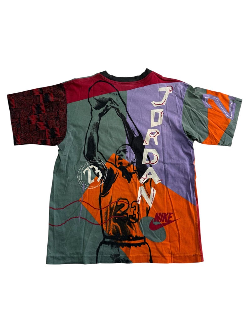 May include: A vibrant t-shirt with a basketball player graphic, the name "JORDAN" printed vertically on the back. The shirt has a patchwork design with orange, purple, green, and red panels, and the Nike logo.
