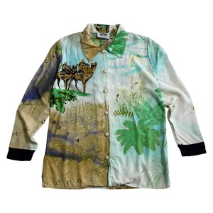 Può includere: Camicia button-down con un design unico con cammelli, mappe e palme. La camicia ha un colletto, maniche lunghe con polsini neri e un mix di colori verdi, blu e beige.