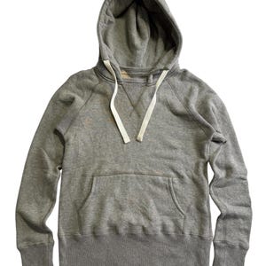 May include: A heather gray hoodie with a drawstring hood and a kangaroo pocket. The sweatshirt has long sleeves with ribbed cuffs and a ribbed hem. White drawstrings are visible.