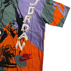 May include: A vintage graphic t-shirt in orange, purple, and green, featuring a basketball player and the word "JORDAN" in white. The Nike logo is visible. The shirt has a crew neck and short sleeves.