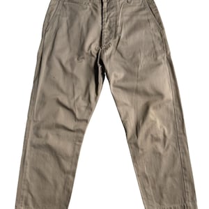 May include: A pair of khaki-coloured trousers featuring a button-fly closure, a waistband with belt loops, two side pockets, and a small coin pocket located just below the waistband on the right side. The trousers have a straight-leg cut.