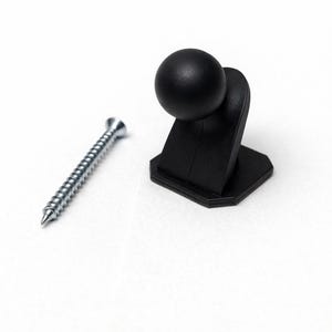 May include: A black cabinet door bumper with a rounded top and a silver screw on a white background. The bumper has a square base and a spherical top. The screw is silver and has a pointed tip.