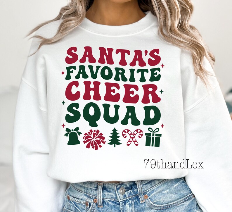 May include: White sweatshirt with the text "SANTA'S FAVORITE CHEER SQUAD" in red and green. The design includes festive icons like a bell, pom-poms, a Christmas tree, candy canes, and a gift box, perfect for the holiday season.
