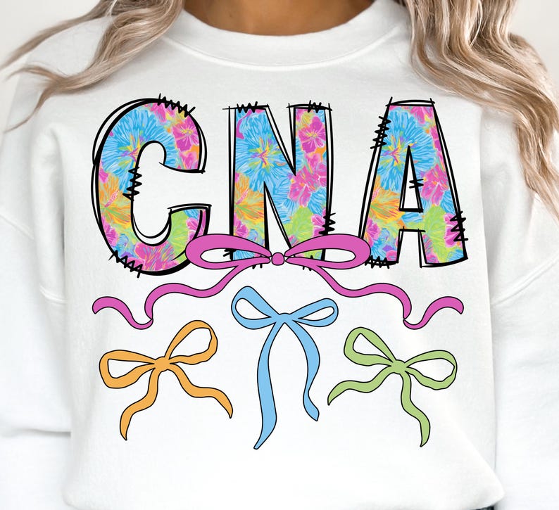 May include: White sweatshirt with the letters "CNA" in a tie-dye floral pattern. The letters are outlined in black with decorative stitching. Below the letters are three bows in pink, blue, and green.