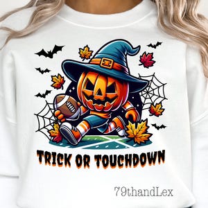 May include: White sweatshirt featuring a cartoon pumpkin wearing a witch hat and football uniform, holding a football. The text "TRICK OR TOUCHDOWN" is below the pumpkin. Bats, leaves, and a spiderweb are also in the design. Halloween themed apparel.