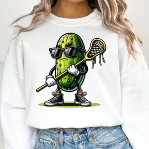 May include: White cropped sweatshirt with a cartoon pickle wearing sunglasses and holding a lacrosse stick. The pickle is green with a yellow and green striped sock.