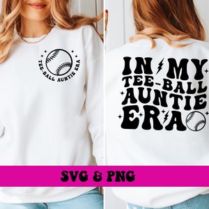 May include: White sweatshirt with black text and baseball graphics. The front features a baseball graphic with the text "TEE-BALL AUNTIE ERA". The back of the sweatshirt has the text "IN MY TEE-BALL AUNTIE ERA" with a baseball graphic.