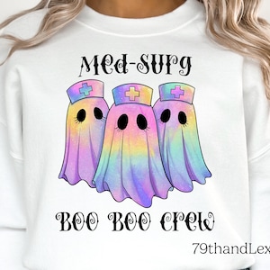 May include: A white sweatshirt featuring a graphic of three iridescent, rainbow-colored ghosts wearing nurse caps with crosses. The text above reads MED-SURG and the text below reads BOO BOO CREW in a black, stylized, decorative font.