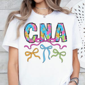 May include: A white ceramic mug with a black handle and the text "But First, Coffee" in a bold, black font. The mug is filled with a dark liquid, likely coffee, and sits on a light-colored surface.