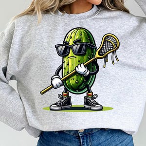 May include: A gray sweatshirt with a cartoon pickle wearing sunglasses and holding a lacrosse stick. The pickle is wearing sneakers and has a green and white striped sock on one foot.