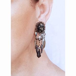 Puede incluir: Un par de pendientes colgantes con una pieza central de patrón negro y marrón y una cascada de cuentas negras, marrones y doradas.