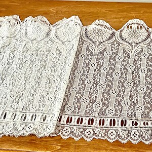 May include: Two pieces of white lace trim with scalloped edges and intricate floral patterns. The lace is delicate and has a vintage feel.