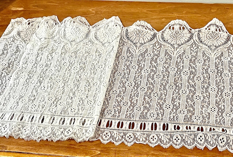 May include: Two pieces of white lace trim with scalloped edges and intricate floral patterns. The lace is delicate and has a vintage feel.