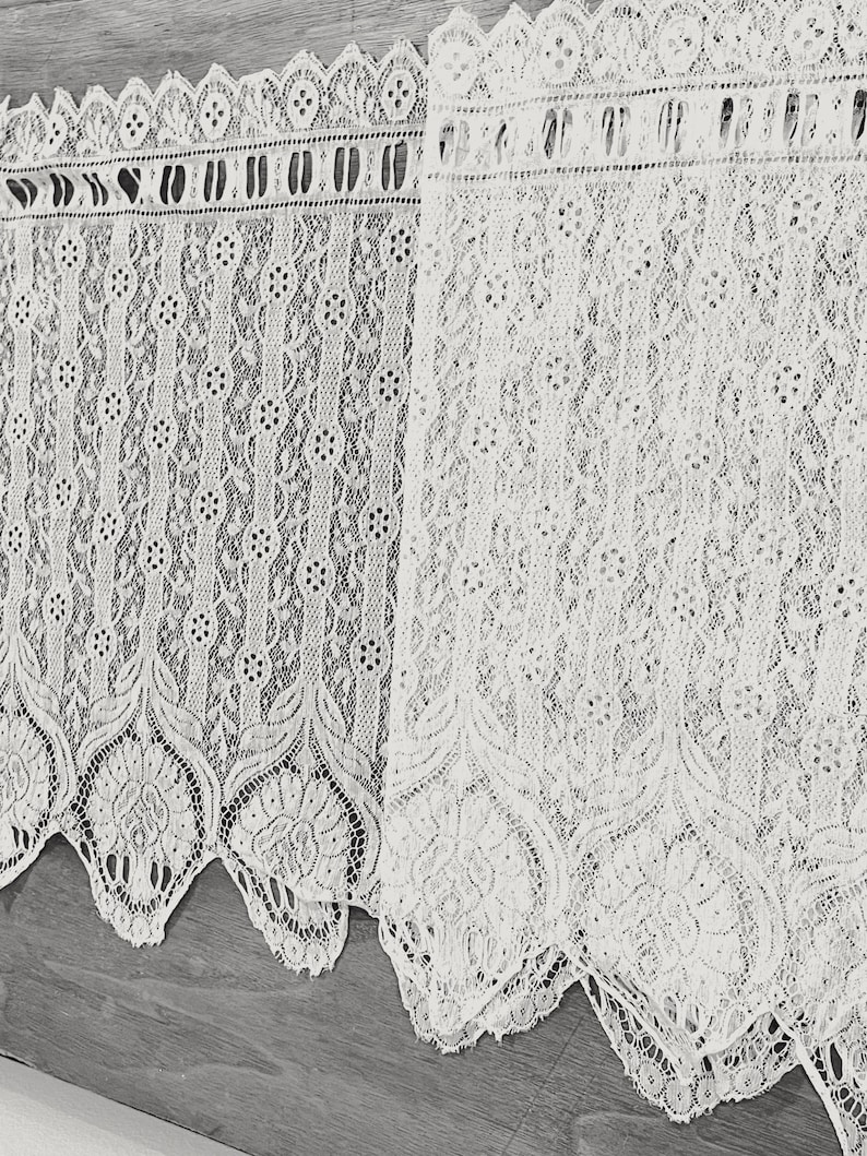 May include: Two white lace curtains with a scalloped edge and a delicate floral pattern.