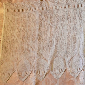 May include: White lace trim with a scalloped edge. The lace has a delicate floral pattern.