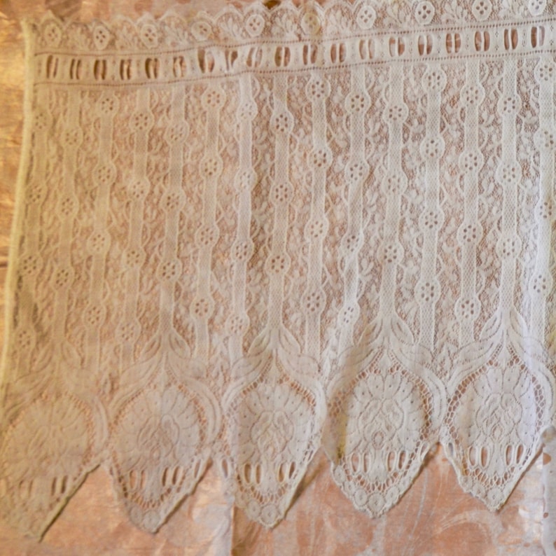 May include: White lace trim with a scalloped edge. The lace has a delicate floral pattern.