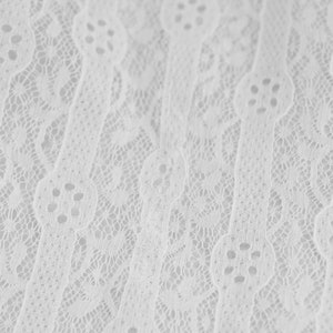 May include: White lace fabric with a delicate, intricate pattern. The lace has a slightly textured surface and a soft, flowing drape.