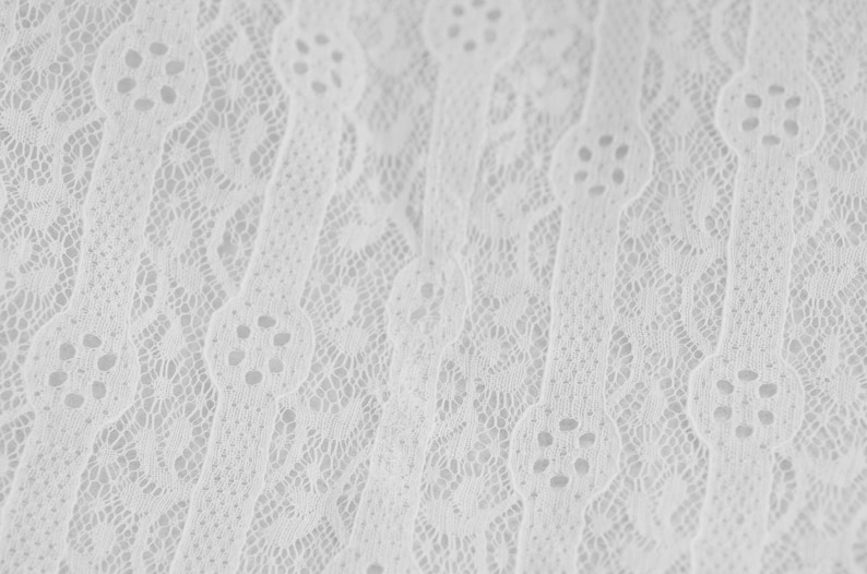 May include: White lace fabric with a delicate, intricate pattern. The lace has a slightly textured surface and a soft, flowing drape.