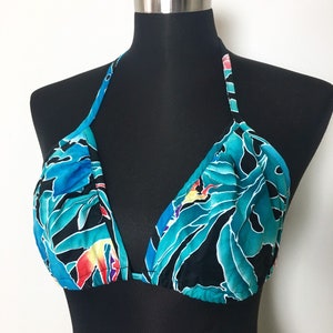 May include: A teal and black halter bikini top with a tropical floral pattern. The bikini top features a triangle shape with adjustable straps and a tie closure. The pattern includes blue, yellow, red, and purple accents.