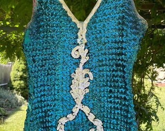 May include: A teal sequined bodysuit with a V-neckline and a decorative white and silver embellishment down the front. The edges are trimmed with a gold-colored material. The garment is hanging on a pink hanger.