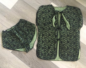 May include: A two-piece lingerie set featuring a black lace overlay over a light green fabric. The set includes a short-sleeved top with a tie closure and matching shorts.