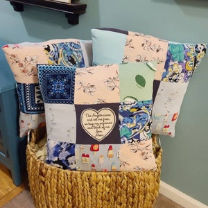 May include: A wicker basket filled with three patchwork pillows. The pillows are made of various fabrics, including floral prints, paisley patterns, and blue and white gingham. One pillow has an embroidered heart with the text "The Angels came and set me free so hug my pajamas and think of me Love Mom".