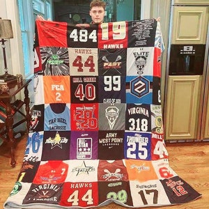 May include: A patchwork quilt made from a variety of sports jerseys. The quilt is made up of squares of different colors and patterns, including red, white, blue, black, and green. The quilt features numbers, team names, and logos from different sports, including lacrosse, football, and basketball. The quilt is a unique and personalized gift for a sports fan.