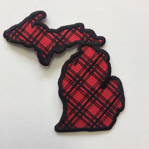May include: Red and black plaid Michigan state outline patch. The patch is made of fabric and has a black outline.