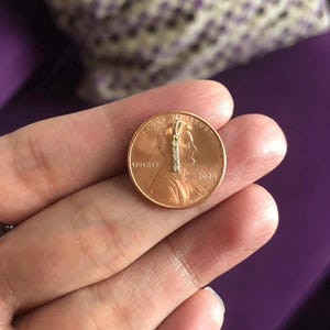 May include: A small gold pendant with a single row of small diamonds, shown next to a 2020 US penny for size comparison.
