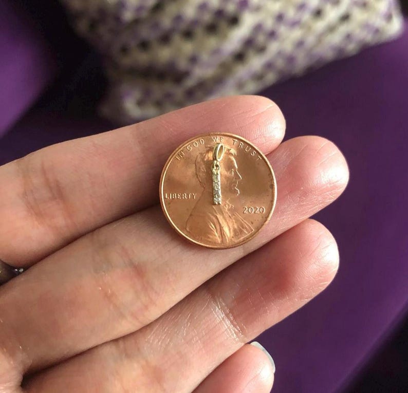May include: A small gold pendant with a single row of small diamonds, shown next to a 2020 US penny for size comparison.