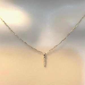 May include: A delicate gold chain necklace with a small pendant featuring a vertical bar of tiny diamonds.